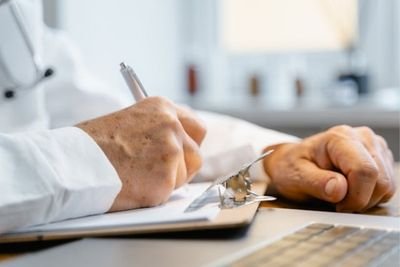 Médico escribiendo notas clínicas en un expediente durante una consulta